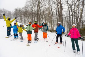Mixed groups of skier and snowboarders standing in a line, waving at the camera
